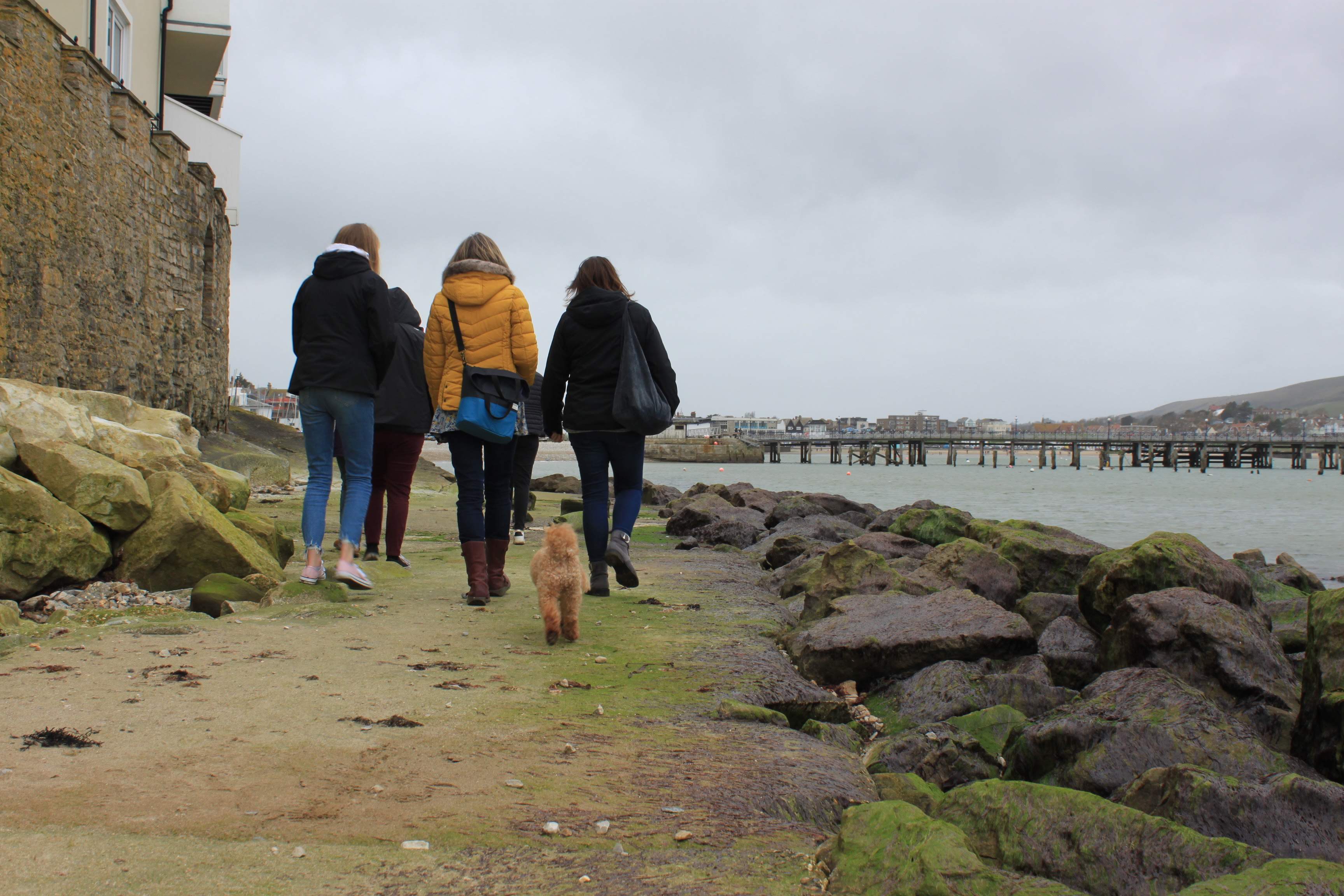 an image of a group of females walking on a path with rocks in a harbour.