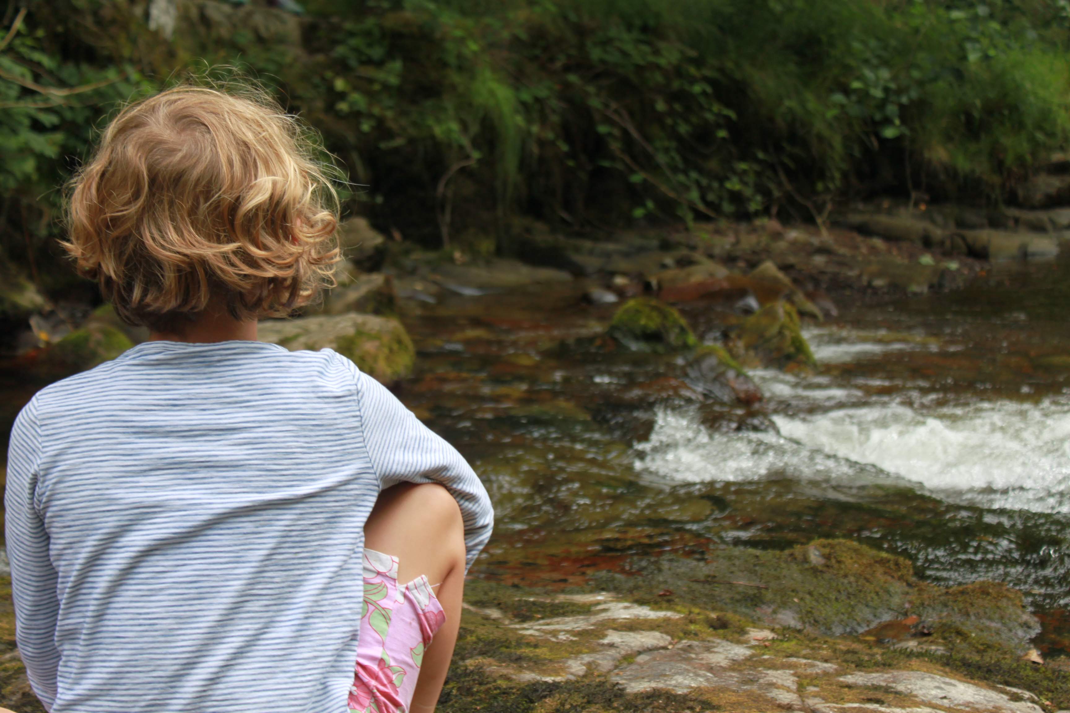 an image of a young female sitting in front of a small stream of water.