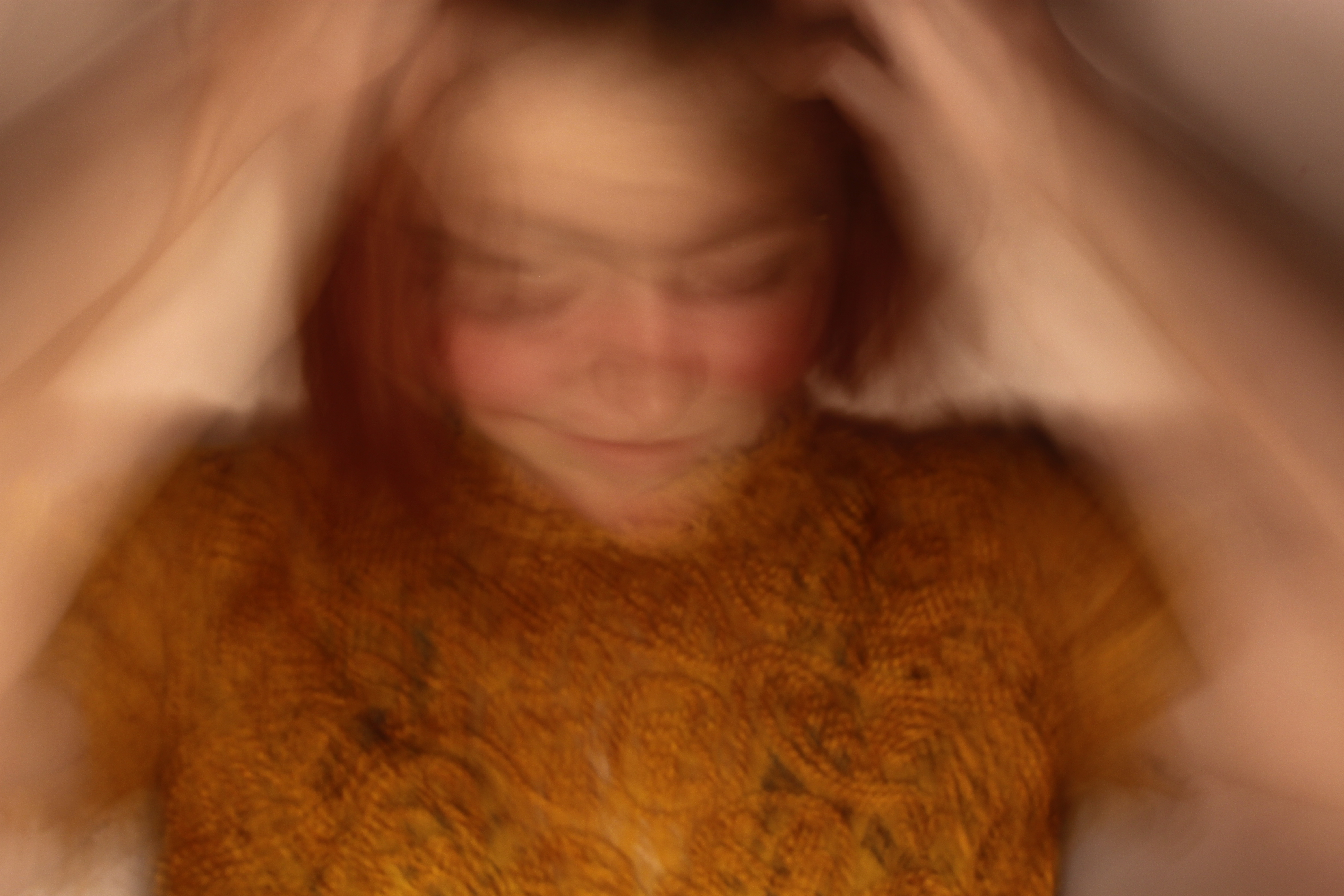 a blurry self portrait of a genderqueer person with their hands in their hair and shaking their head.