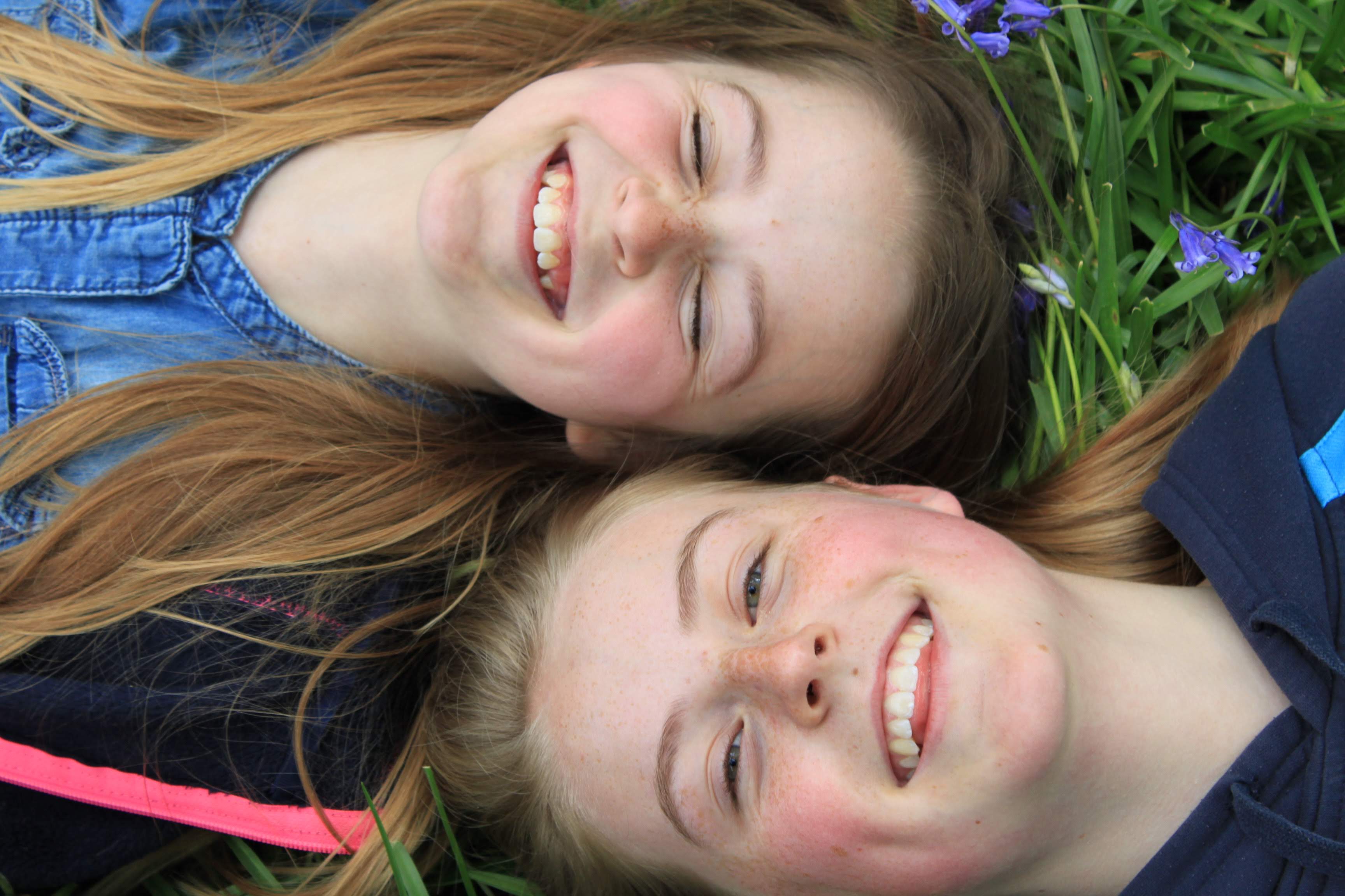 image of two young white females laying in bluebells with their heads next to each other and similing