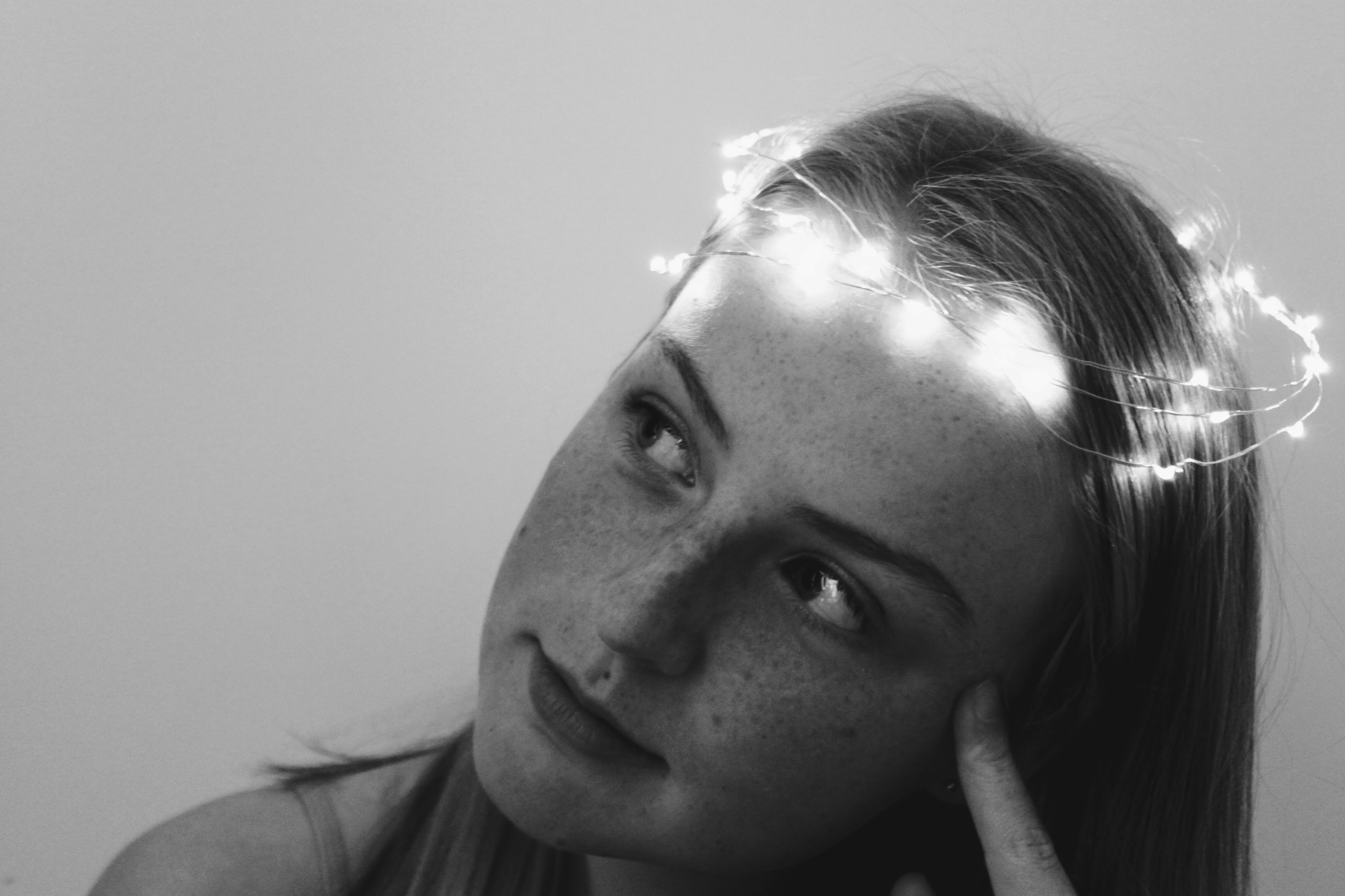 a black and white image of a teenager with fairylights in a ring around her head looking off into the distance.