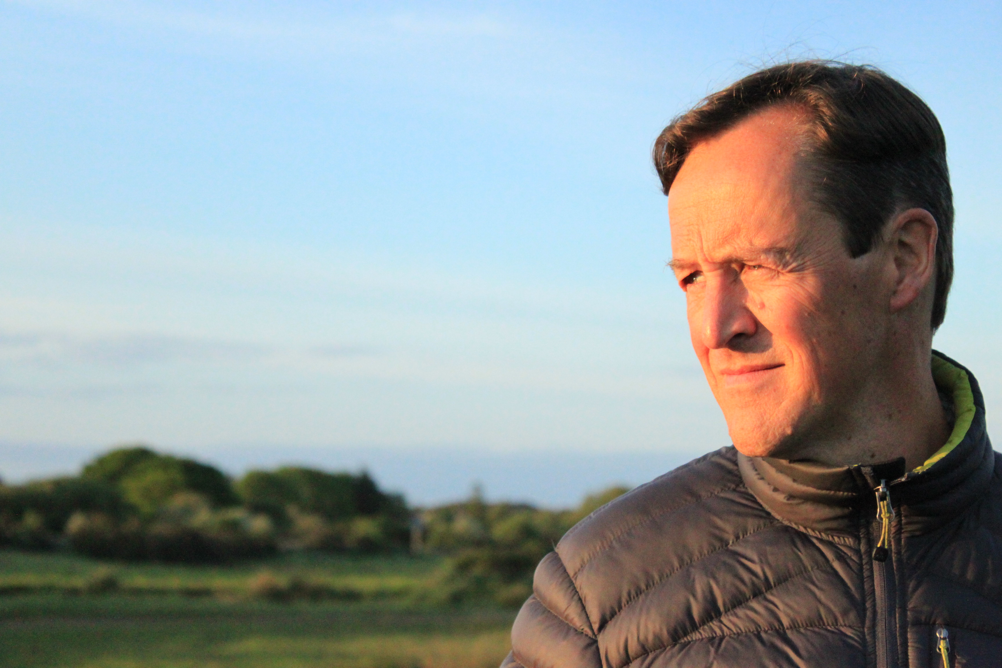 an image of a white middle age man who is staring into the distance with a golden glow lighting up his face.