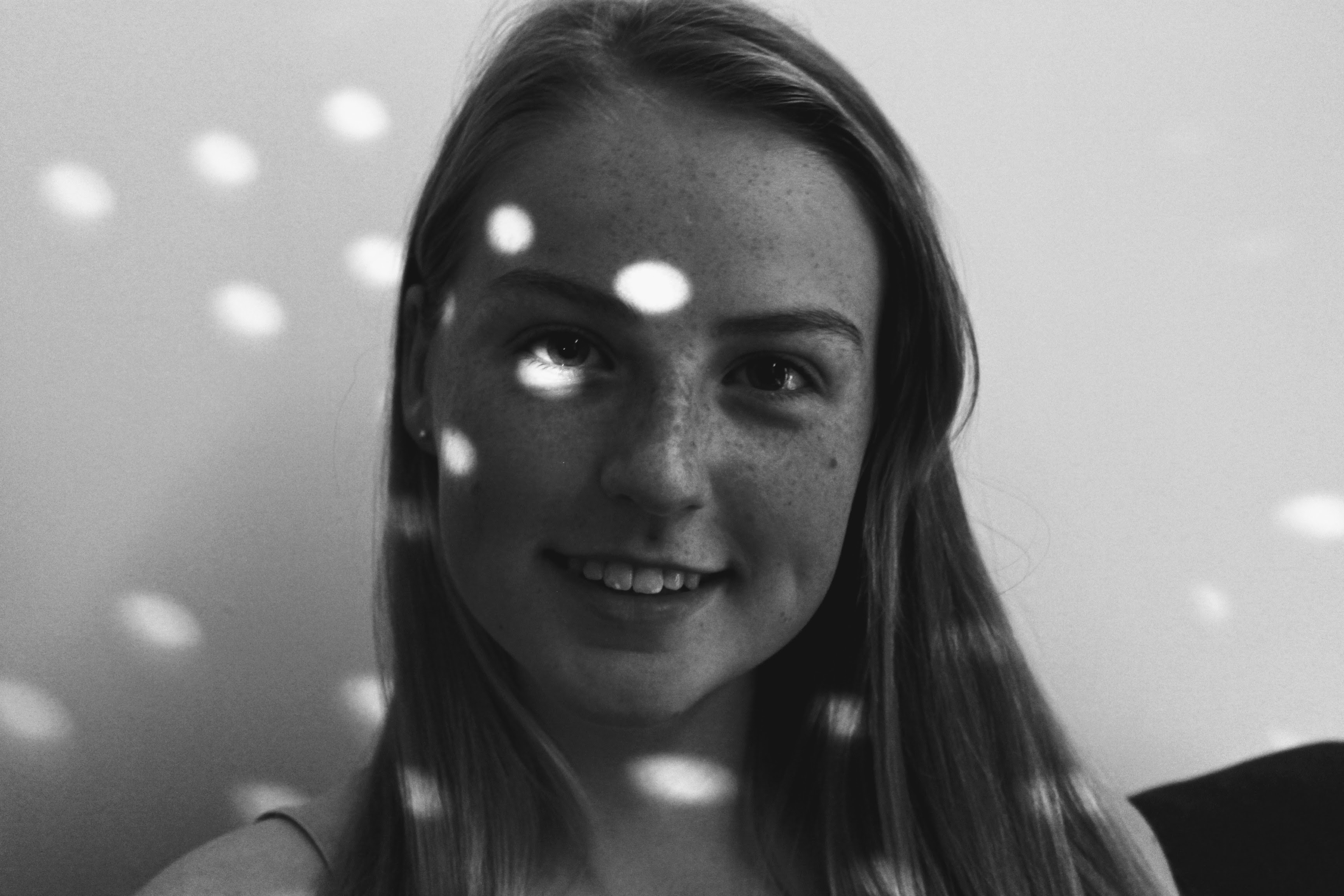 photograph of a white teenager with freckles who is similing into the camera with light circles on her face.