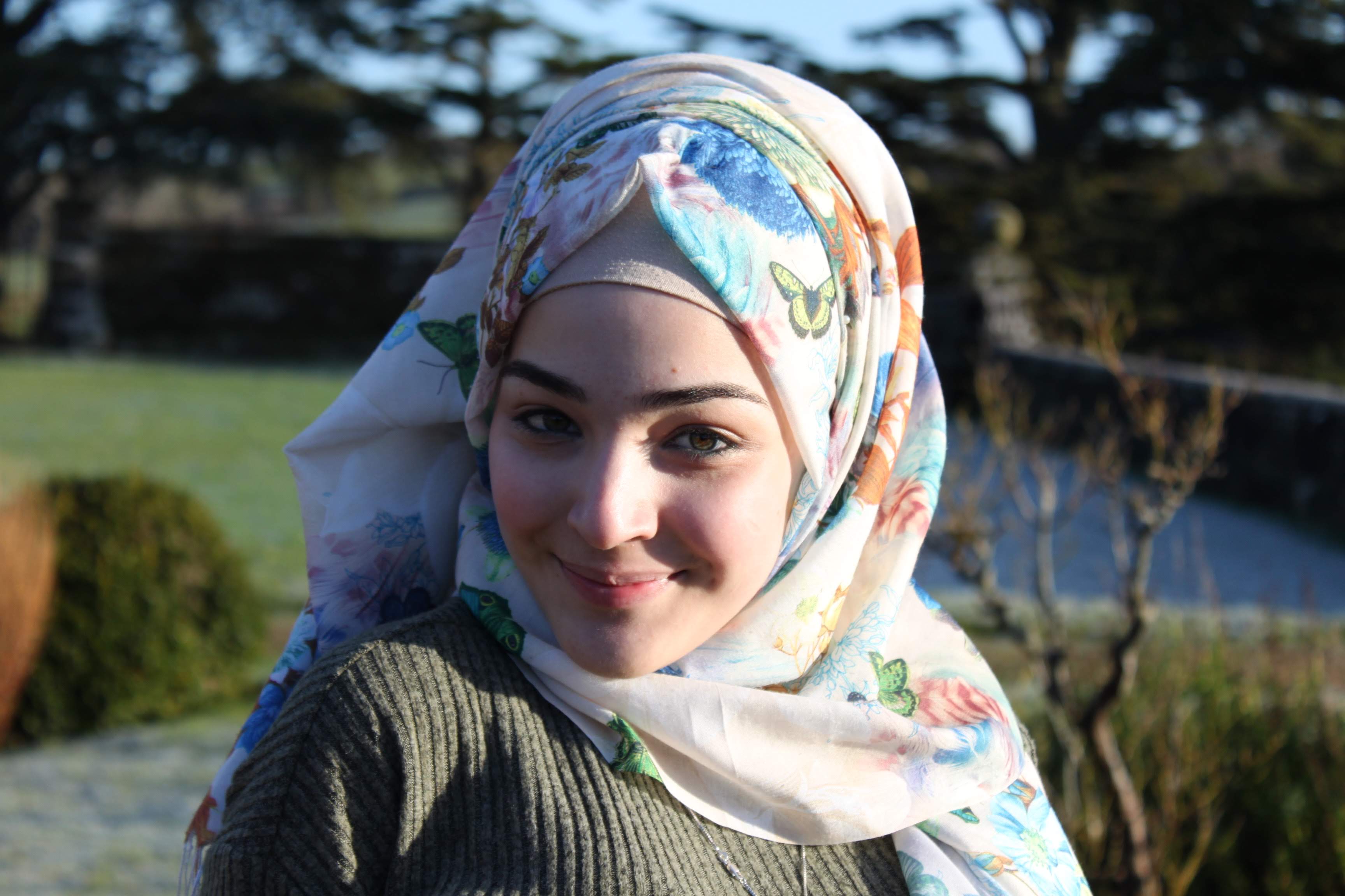 a headshot of a muslim teenager who is wearing a hijab and smiling into the camera.